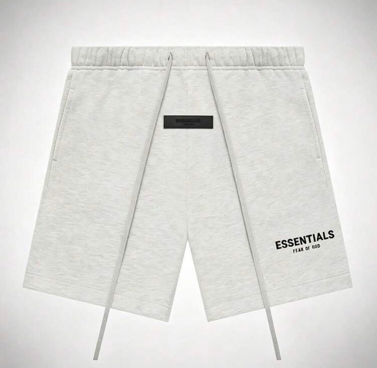 Light heather gray sweat shorts with a black rectangular patch on the front and 'ESSENTIALS FEAR OF GOD'